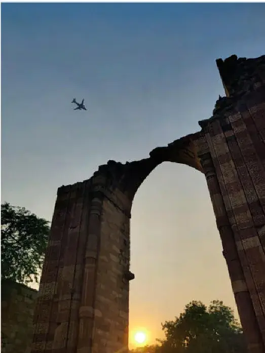 A broken arch at sunset with an aircraft overhead